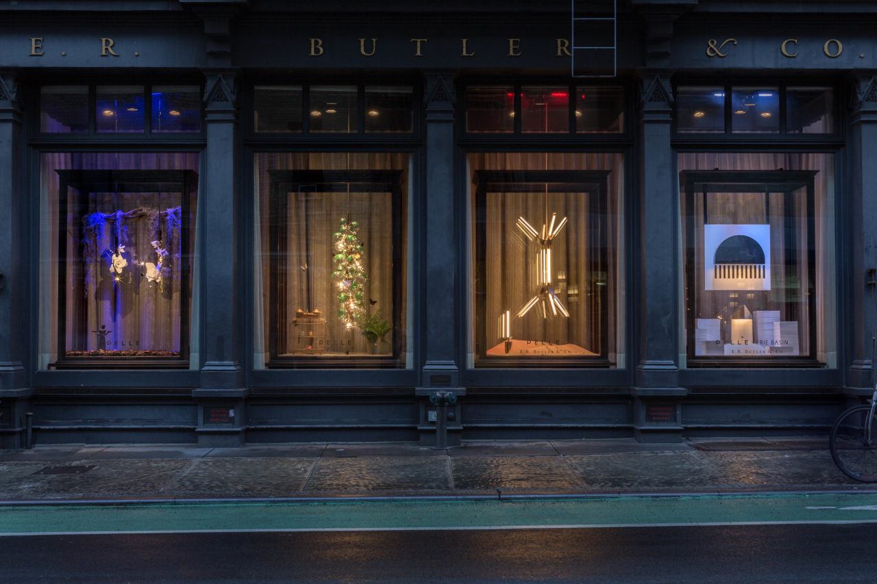 Street view of four shop windows illuminated at night. Pelle’s fixtures illuminate each window, with each window having a different fixture and theme.